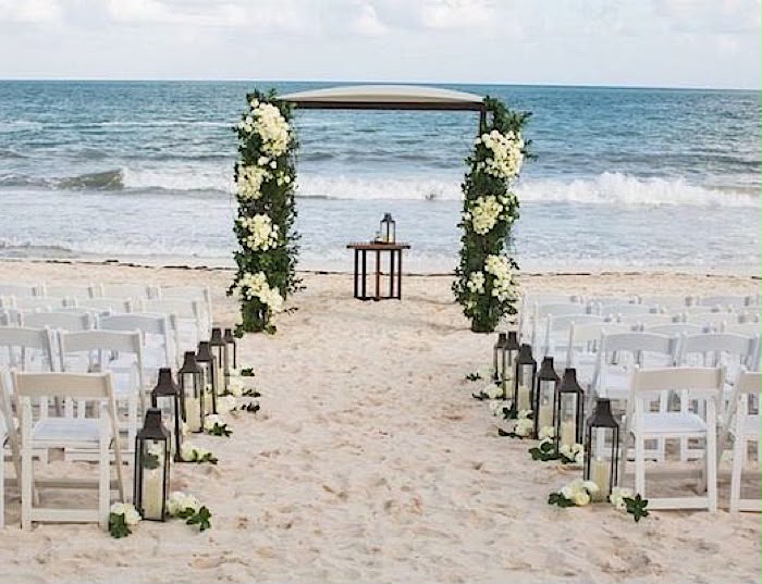 Beachfront wedding ceremony setup with white chairs and floral arch